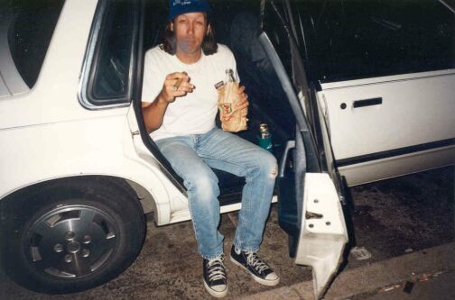 Bryan, smoking a cigar and drinking from a bottle in a brown paper bag